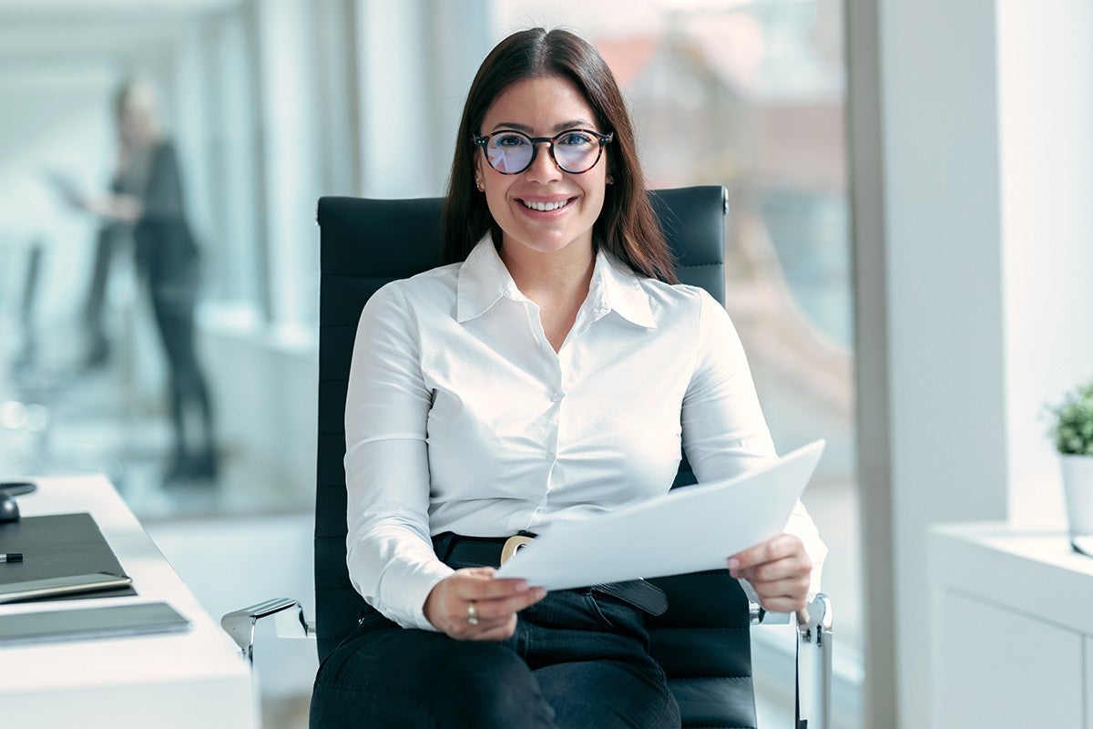 Shot of beautiful business woman holding some documents while looking at camera in modern startup office.; Shutterstock ID 2120500814; purchase_order: -; job: -; client: -; other: -
